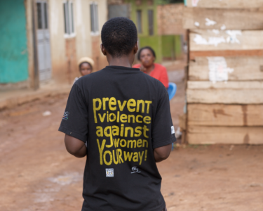 Picture of a man standing backing the camera and wearing a black shirt that reads "prevent violence against women your way"